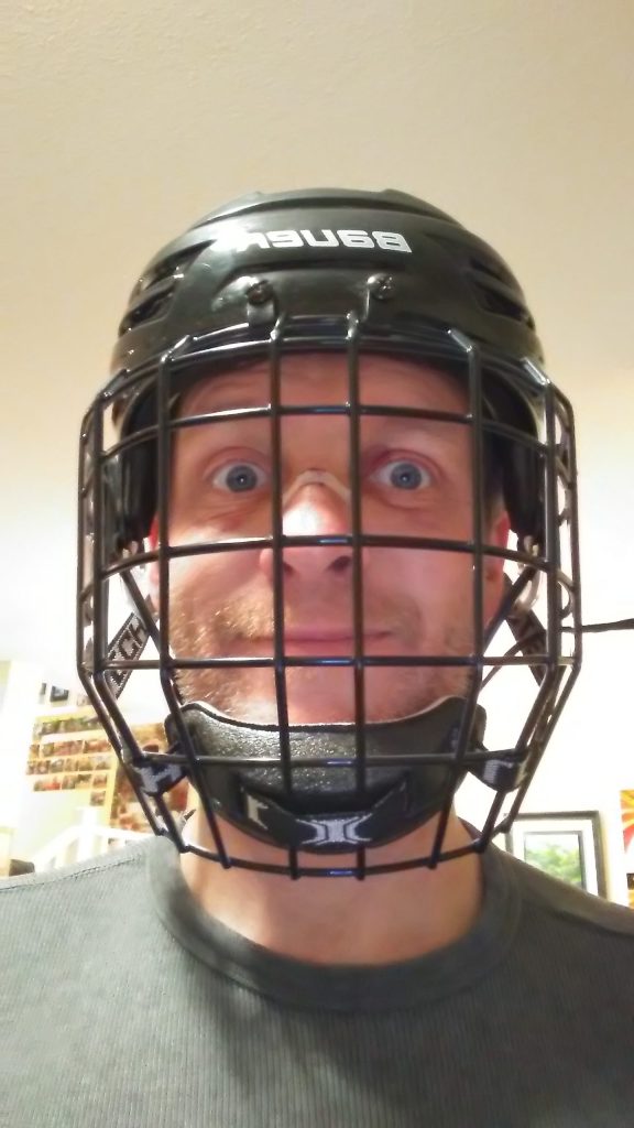 Mark wearing a hockey helmet and mask with bandaid on cut nose